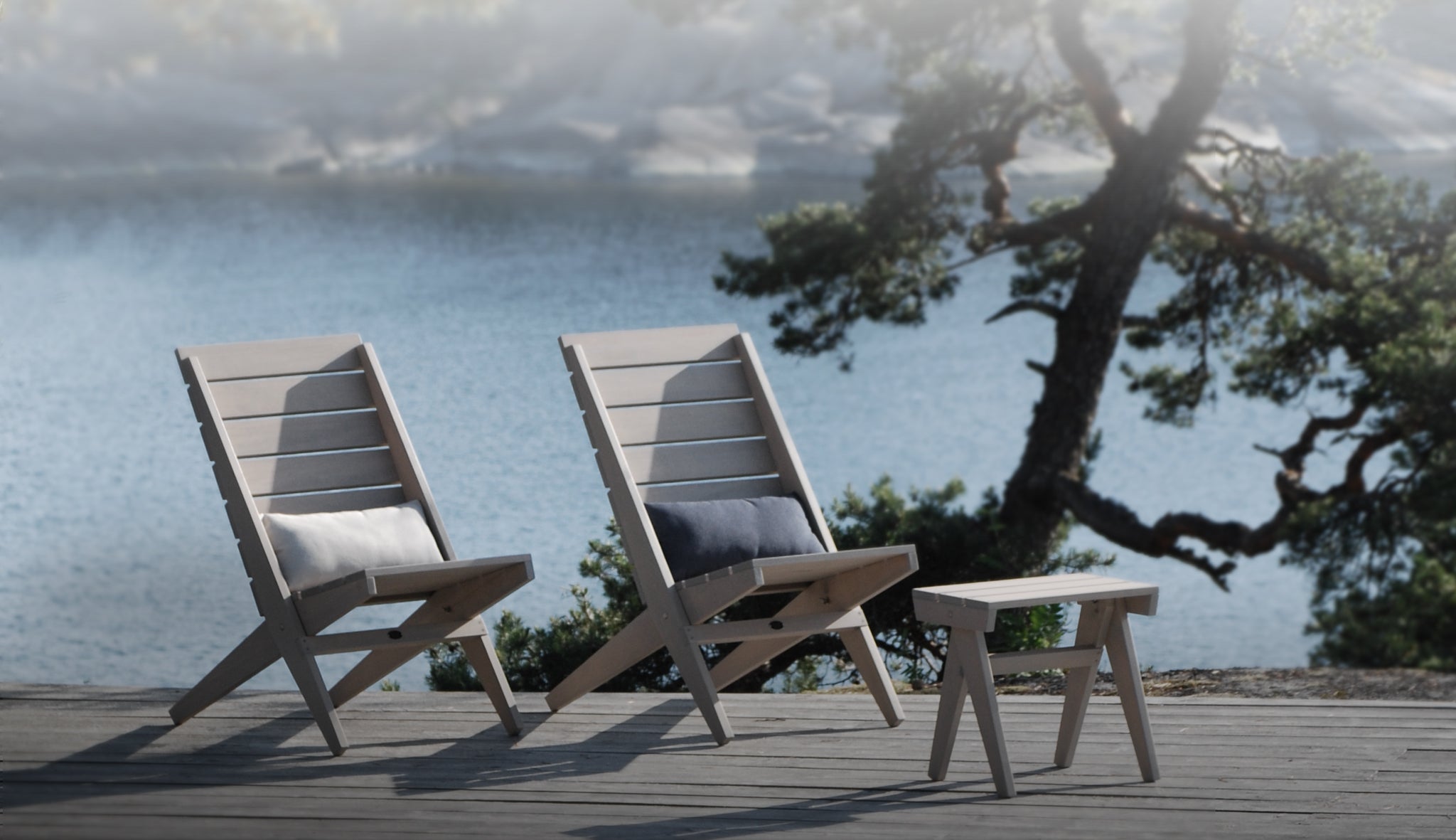 Harmaat puiset taitettavat lepotuolit ja jakkara – skandinaavinen ulkokalustesarja, sijoitettu rantaterassille merinäköalalla.