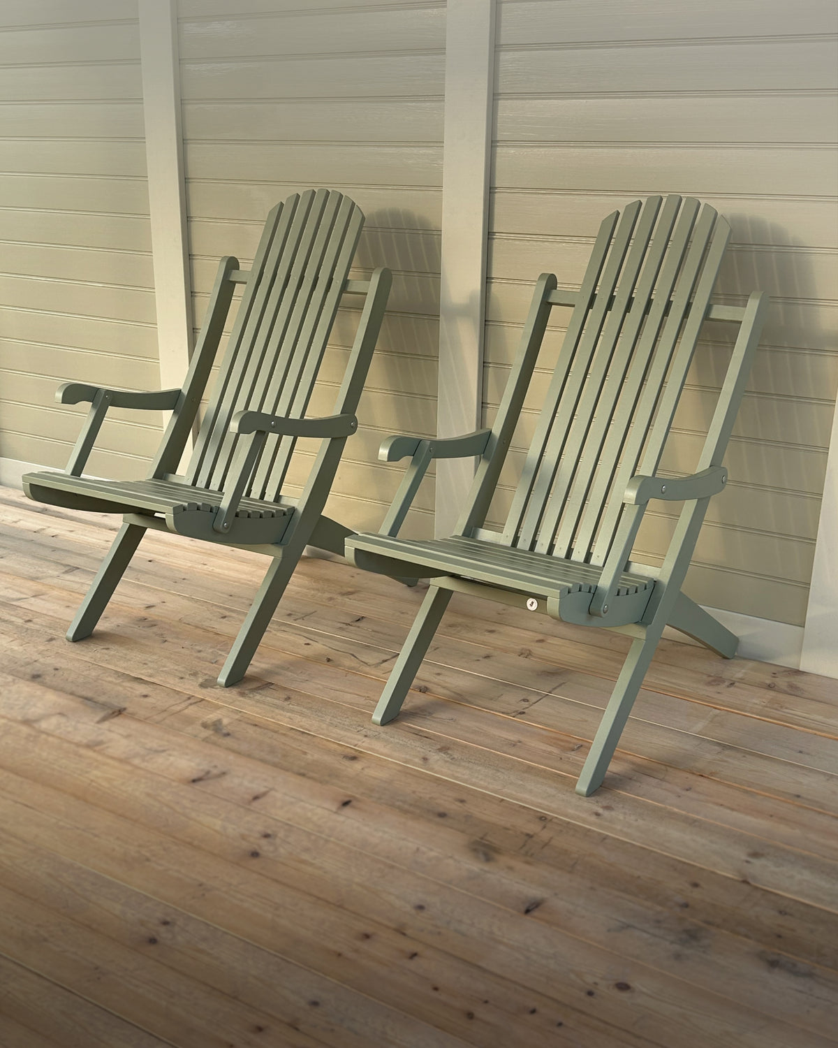 Two green Adirondack chairs on a wooden deck.