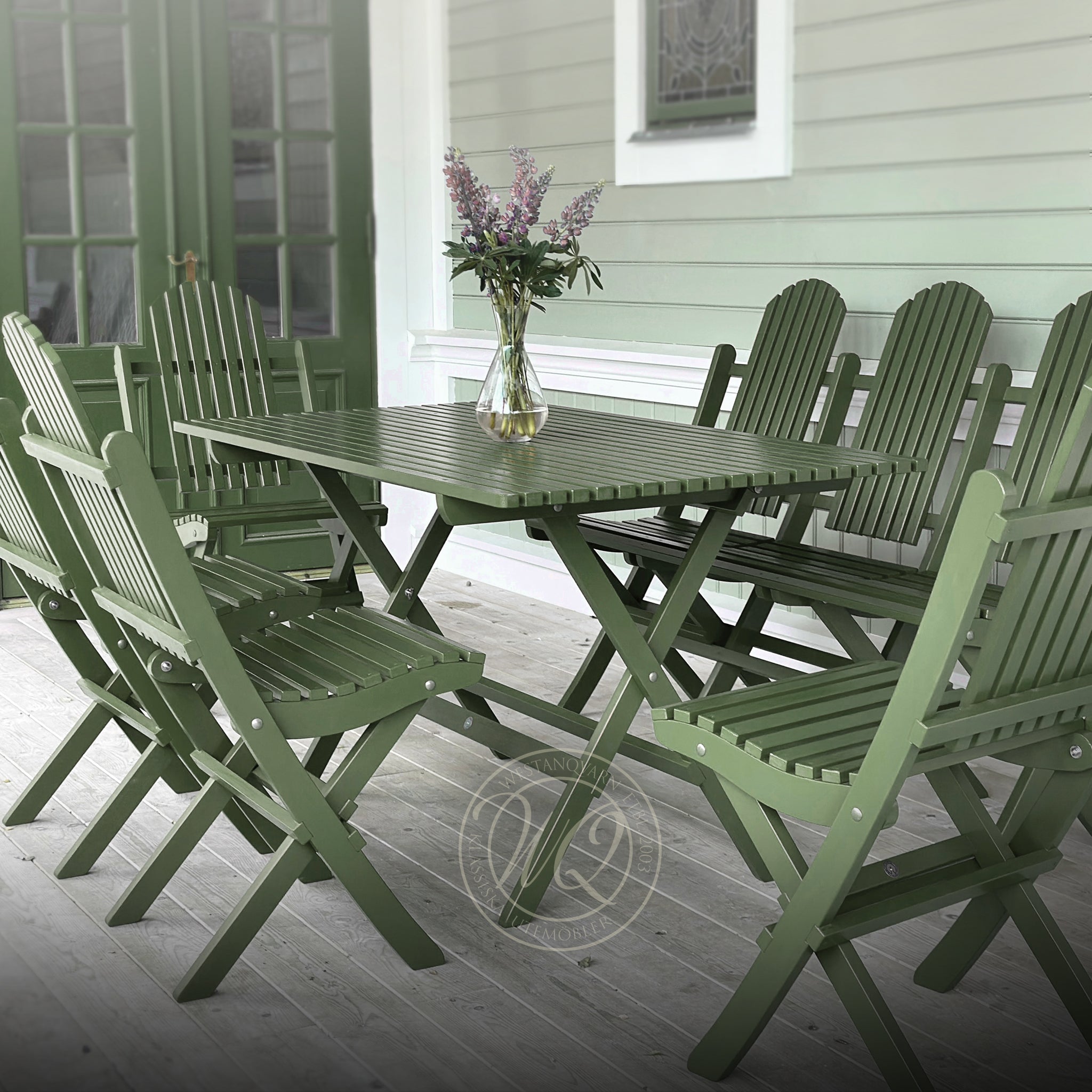 Gröna hopfällbara trädgårdsmöbler i trä – klassiskt matbord med matchande stolar, placerat på en sekelskiftesveranda med gråmålade trägolv.